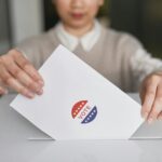A person casting a vote by placing a ballot into a ballot box, symbolizing democratic participation.