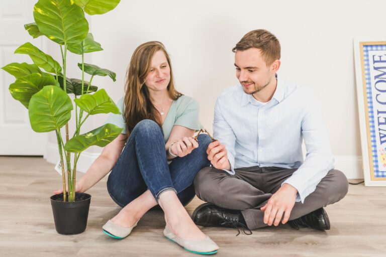 A happy couple sitting on the floor with house keys and a potted plant in their new home.