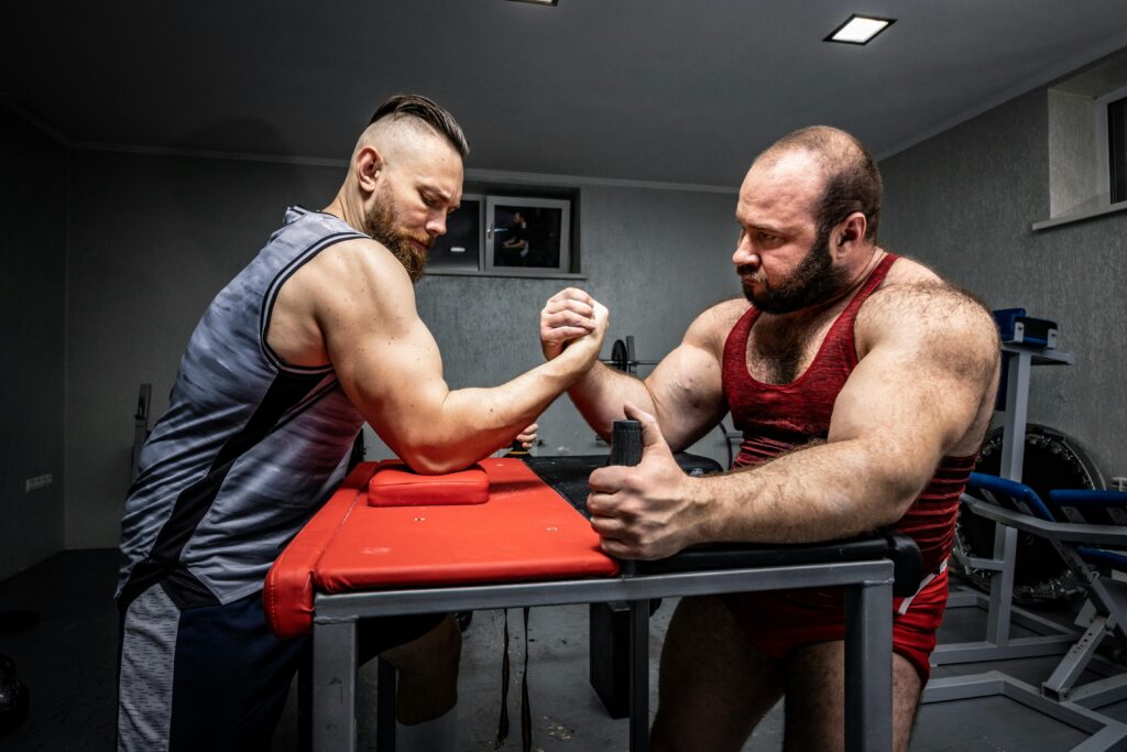 Two muscular men engage in a tense arm wrestling contest at a gym, showcasing strength and competition.