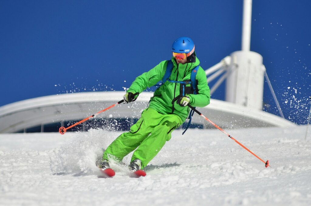 A skier in vibrant gear carves through fresh snow on a sunny winter day.