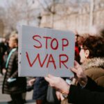 Crowd of people in a peaceful protest holding a 'Stop War' sign outdoors.