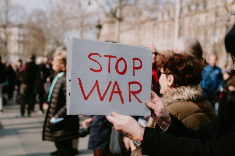 Crowd of people in a peaceful protest holding a 'Stop War' sign outdoors.