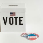 White ballot box with USA flag and 'I Voted' badges on a white background.
