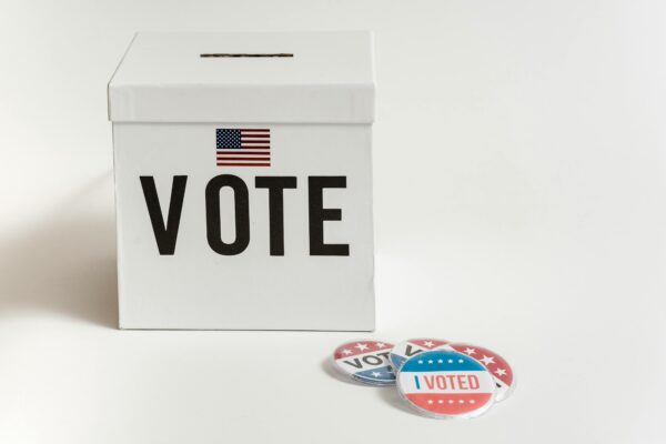 White ballot box with USA flag and 'I Voted' badges on a white background.