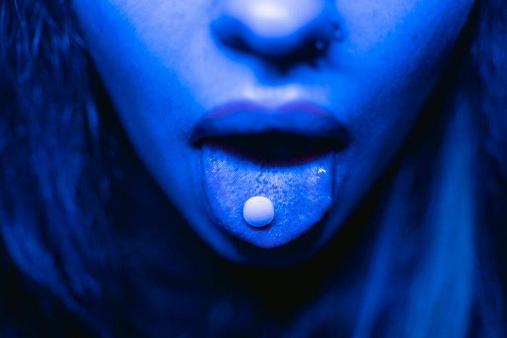 Dramatic close-up of a person with a tablet on their tongue in blue lighting.