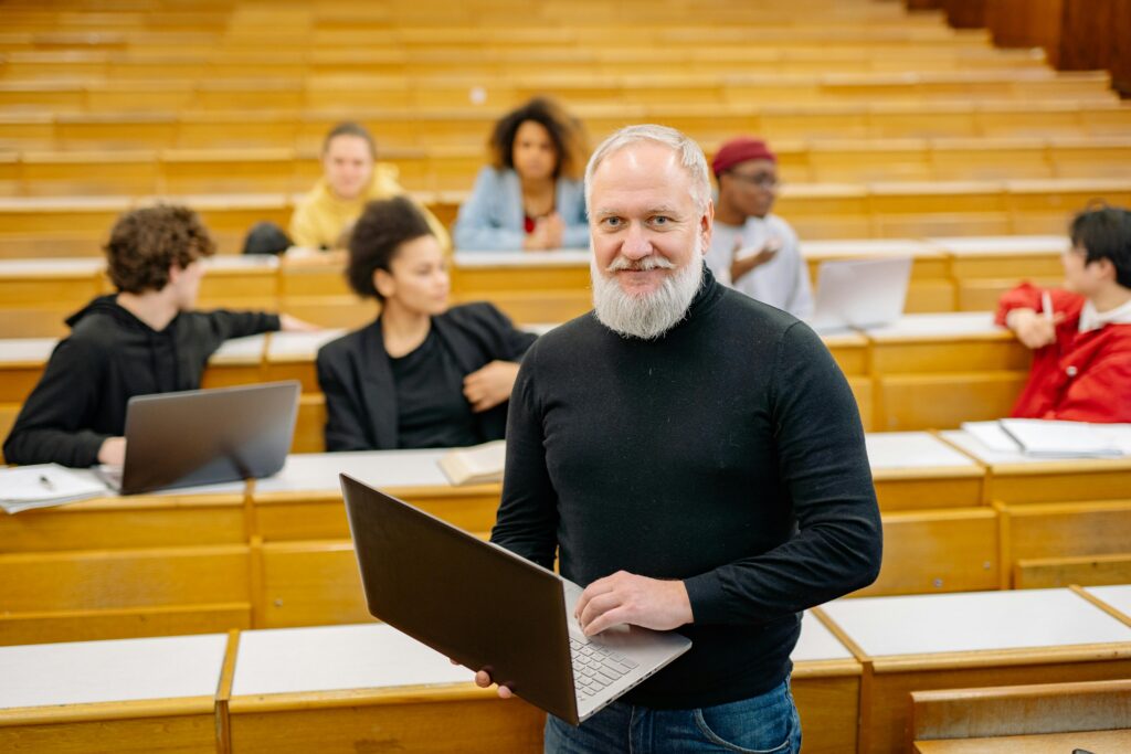 Diverse group of university students in a lecture hall with a professor holding a laptop, promoting education.
