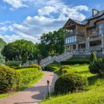 Stunning wooden manor surrounded by well-manicured gardens and vibrant trees under a clear blue sky.