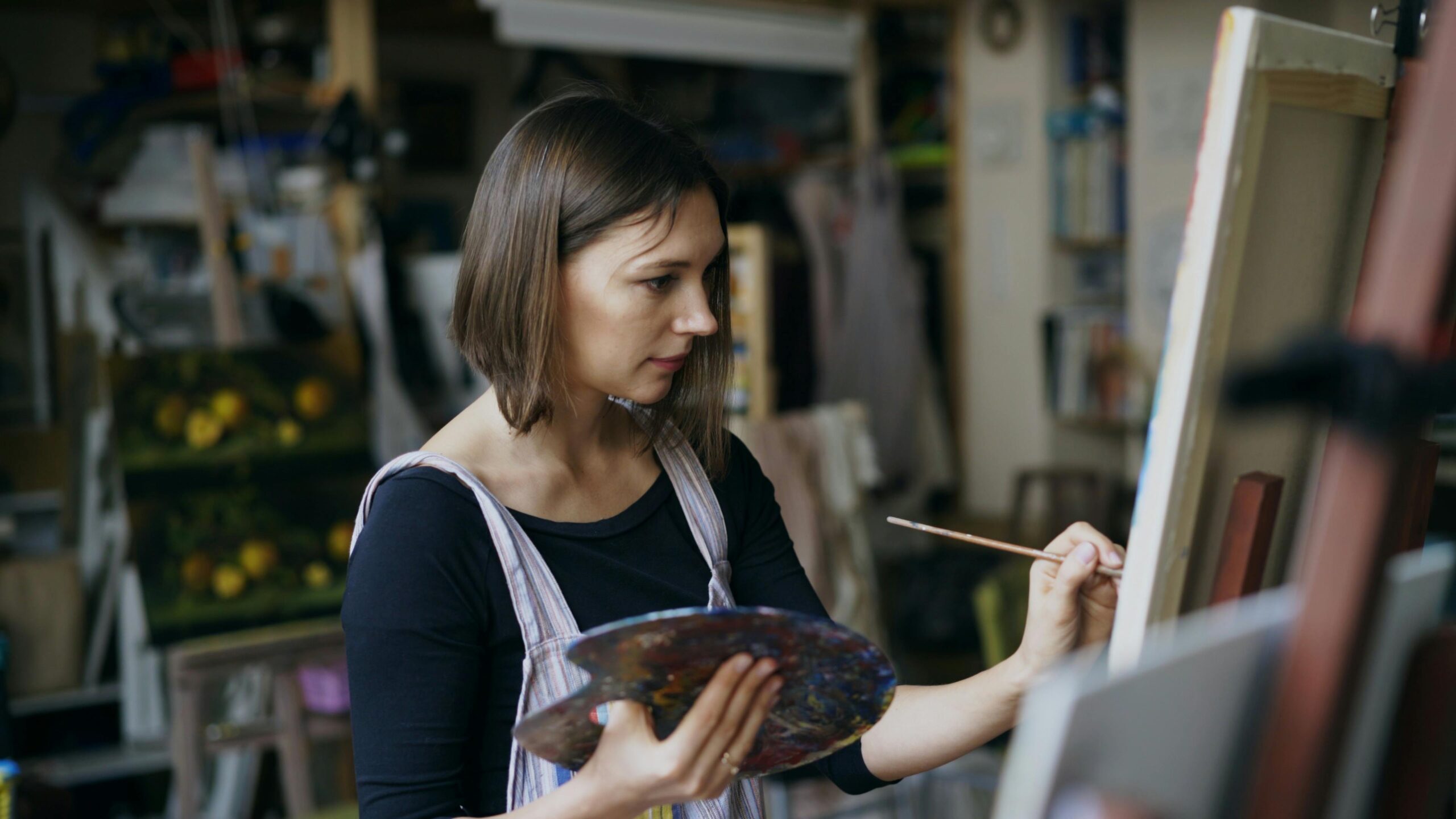 Female artist painting with focus in an art studio, holding a palette.